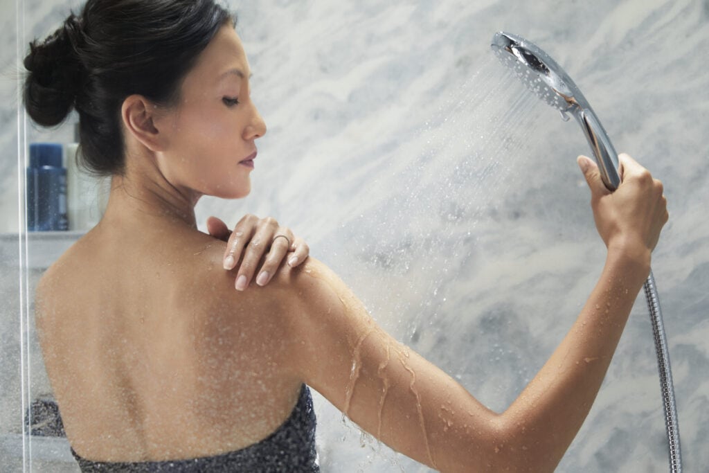 woman showering with handheld showerhead|bath salt|bath towels|essential oils